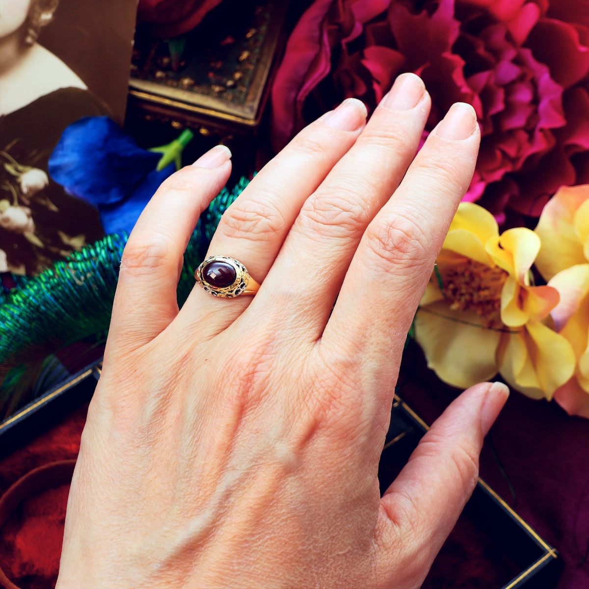 Hand wearing a ring with a red gemstone against a colorful floral background