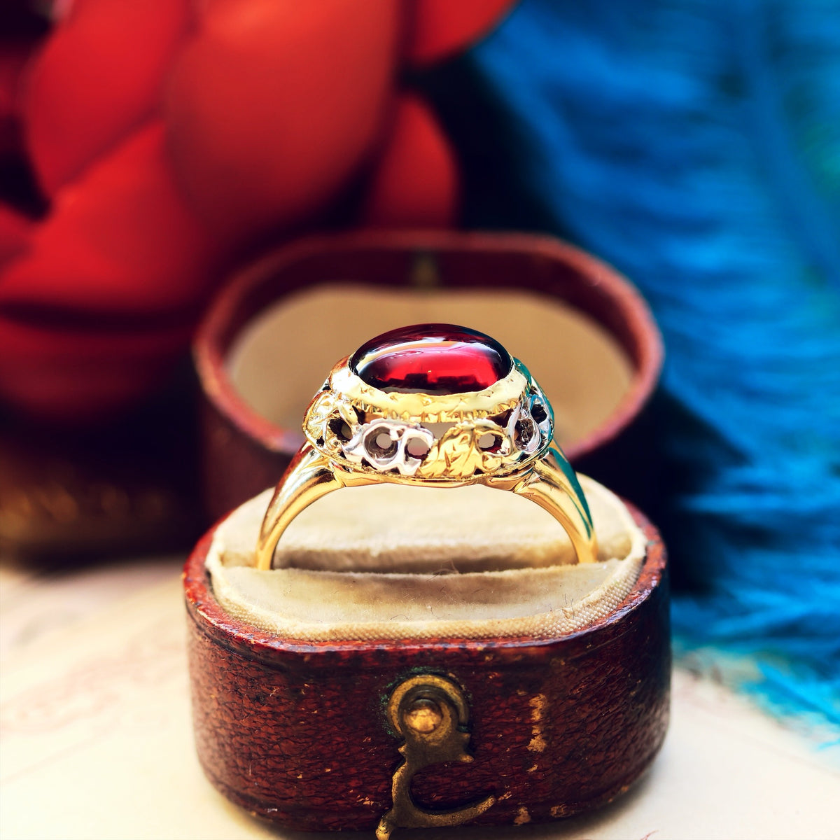 Gold ring with a red gemstone in an open jewelry box against a colorful background