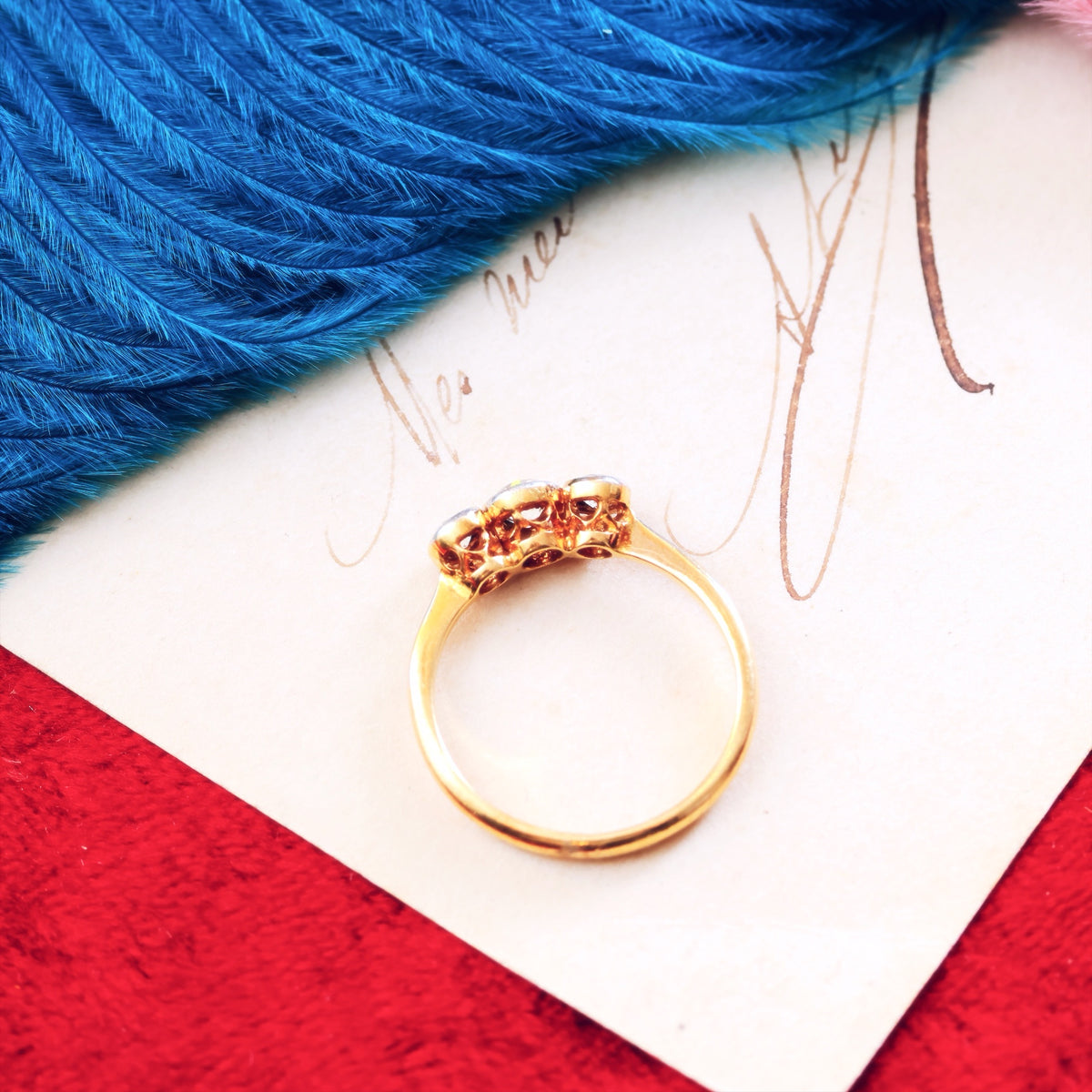 Gold ring on a white card with blue feathers and red fabric