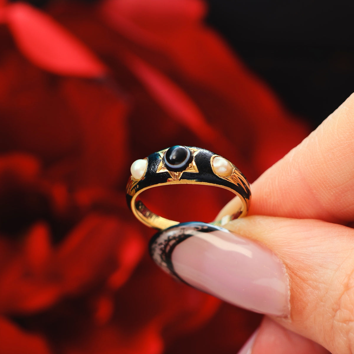Gold ring with black and white stones held by a hand against a red floral background